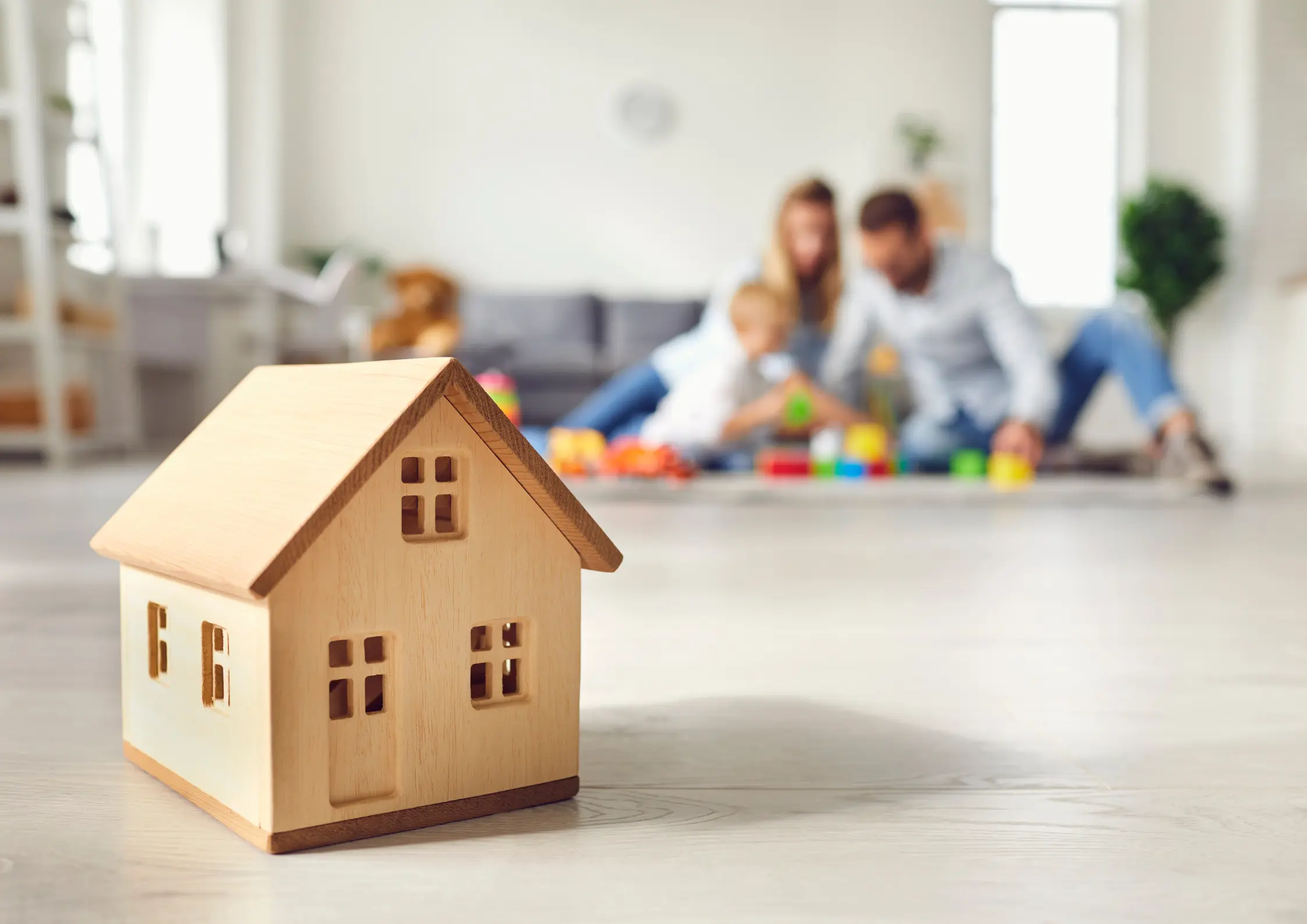 Estate Planning in Cheektowaga, NY Wooden model house with a young family in the background, representing protecting your home and family through estate planning in Cheektowaga, NY